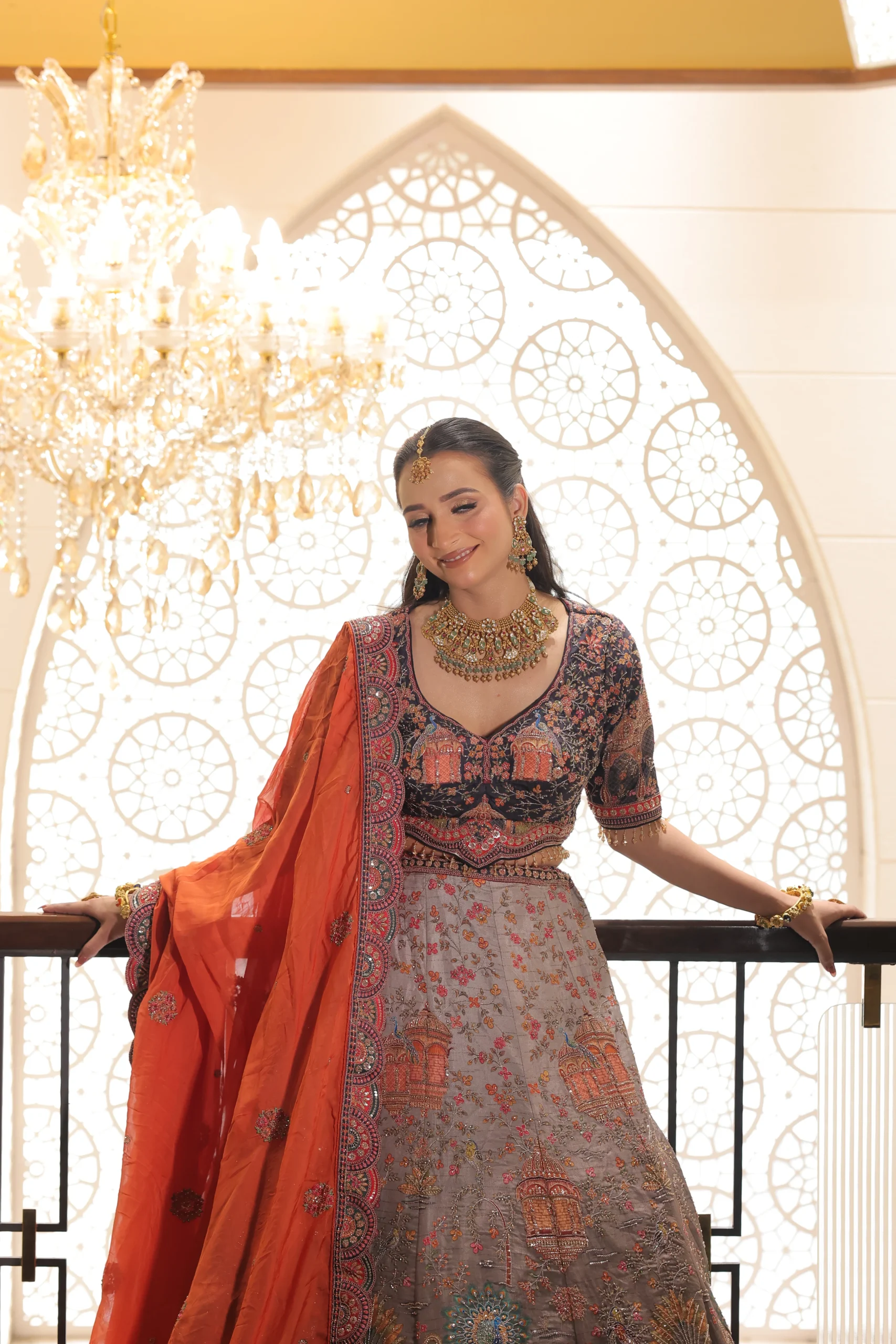 Model in an orange printed RP Dalmia lehenga under a white arch
